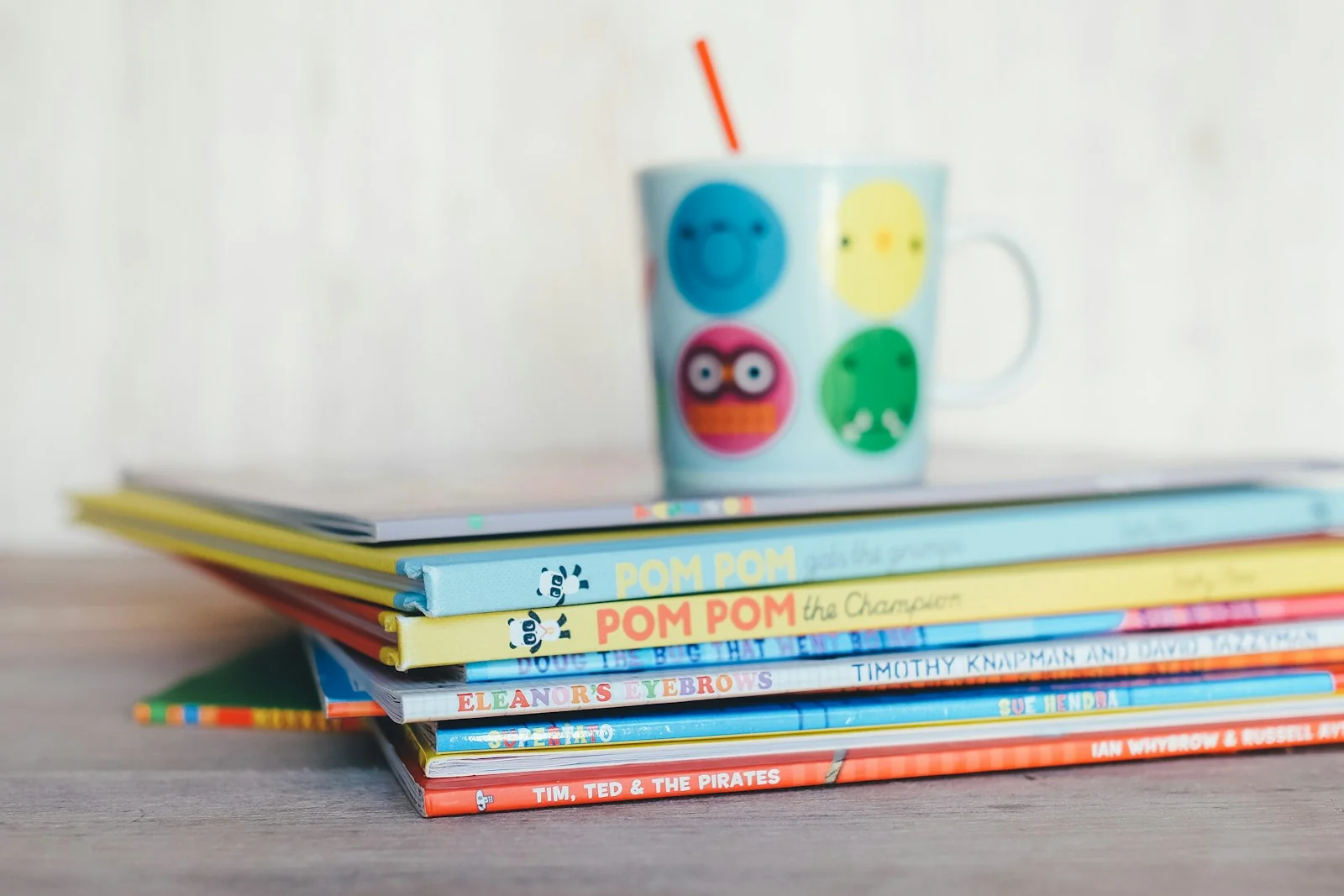 A stack of colorful children's books with a mug on top