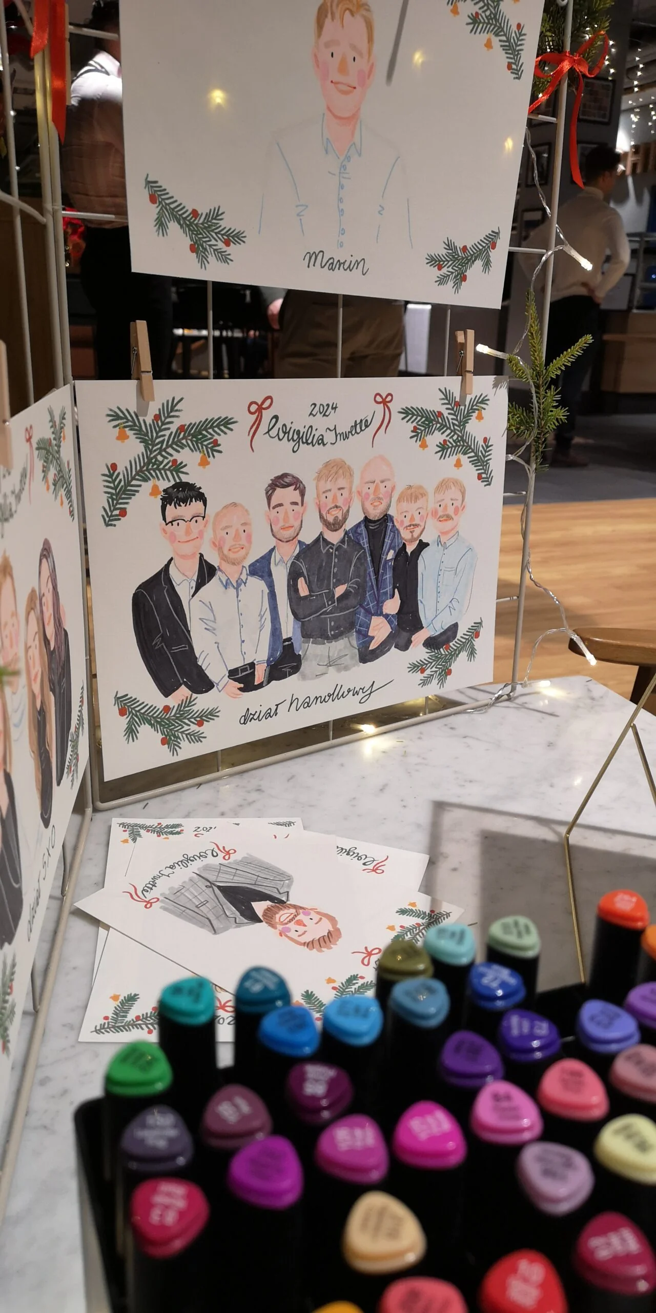 Live painting na evencie firmowym - ilustrowany portret zespołu na stojaku i markery na stole
