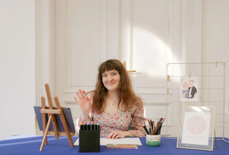 Ilustratorka przy stanowisku z markerami i akwarelowymi portretami na zamówienie