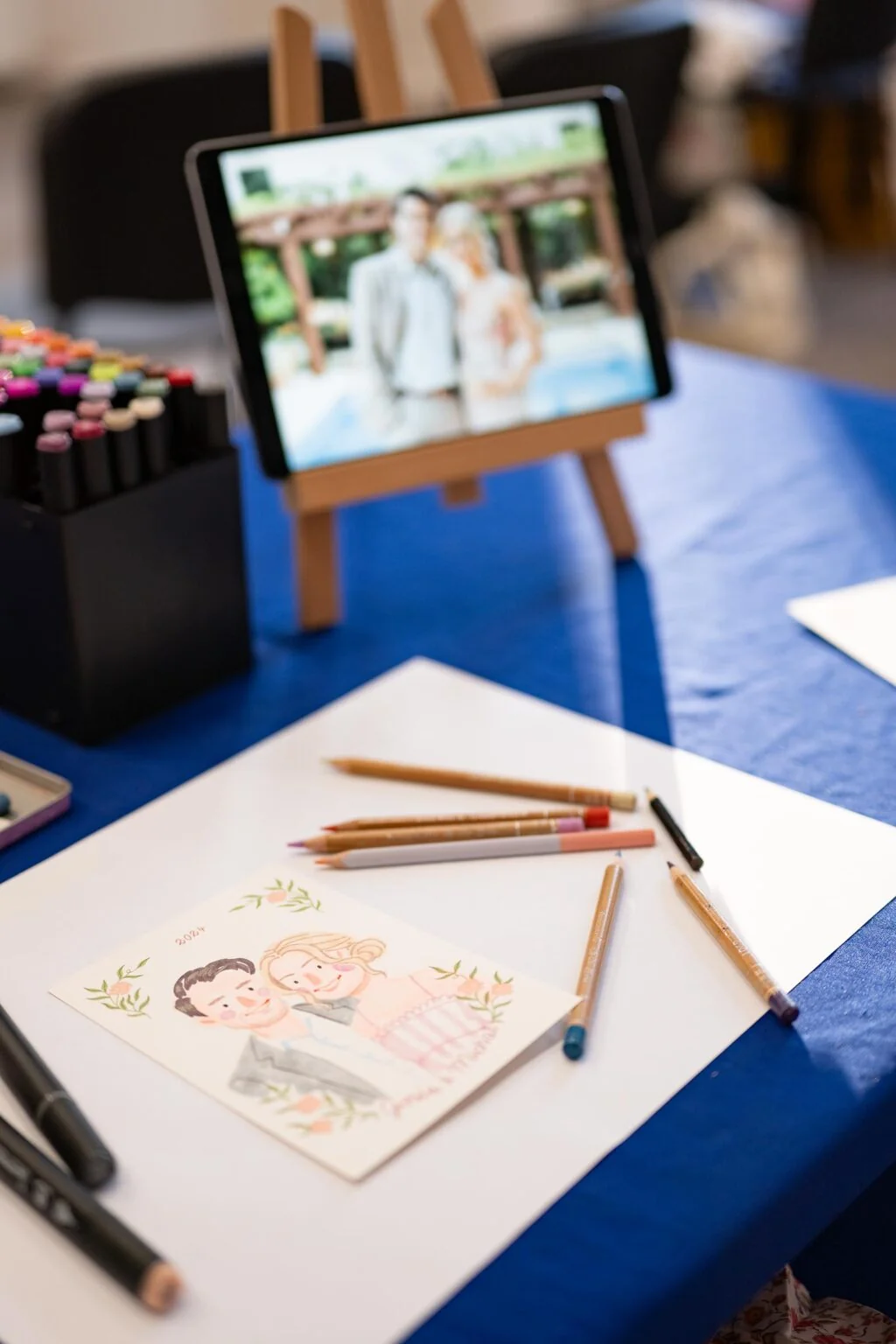 Live painting na evencie - malowany akwarelowy portret pary na podstawie zdjecia z tabletu, obok markery i kredki